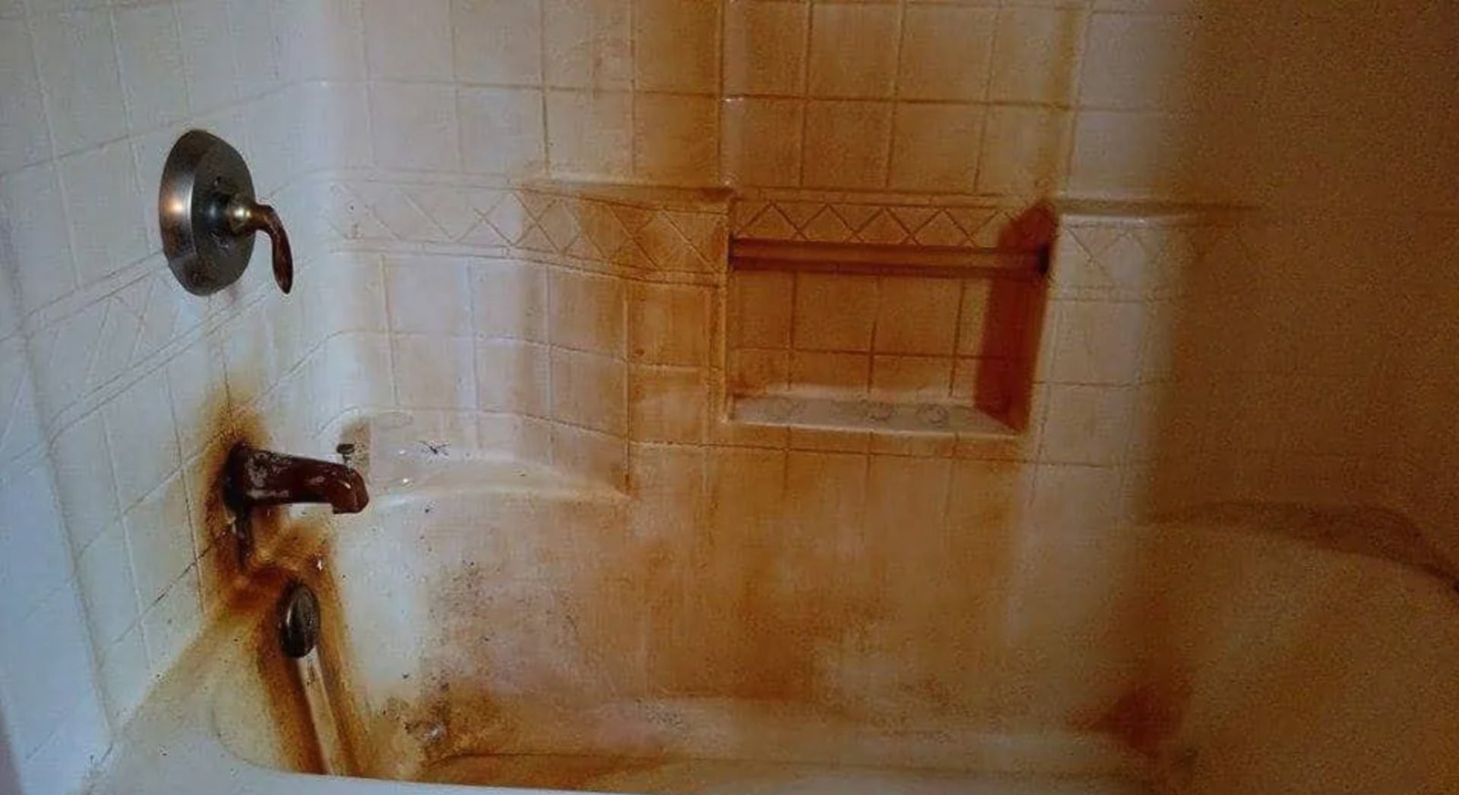 Bathtub and shower fixtures heavily stained orange and brown from iron in well water